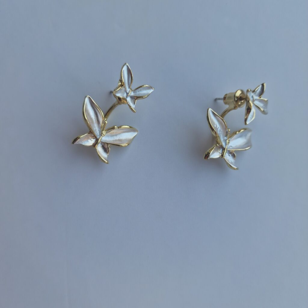 Double butterfly gold earrings with pearl detail on a white background.