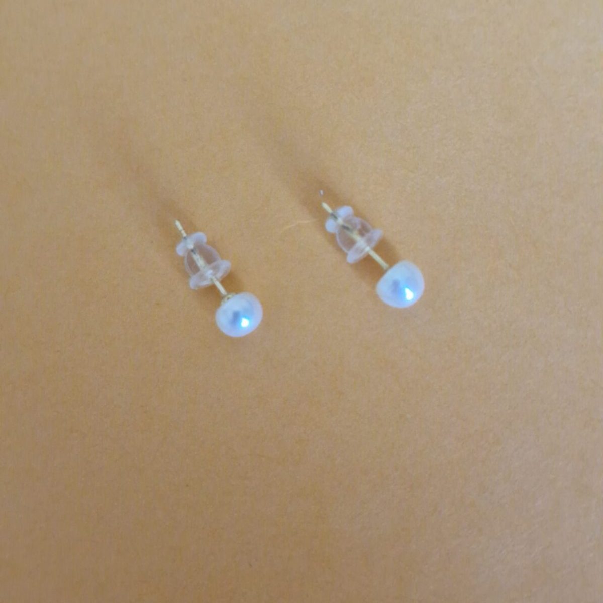 Two stud pearl silver earrings on a orange background